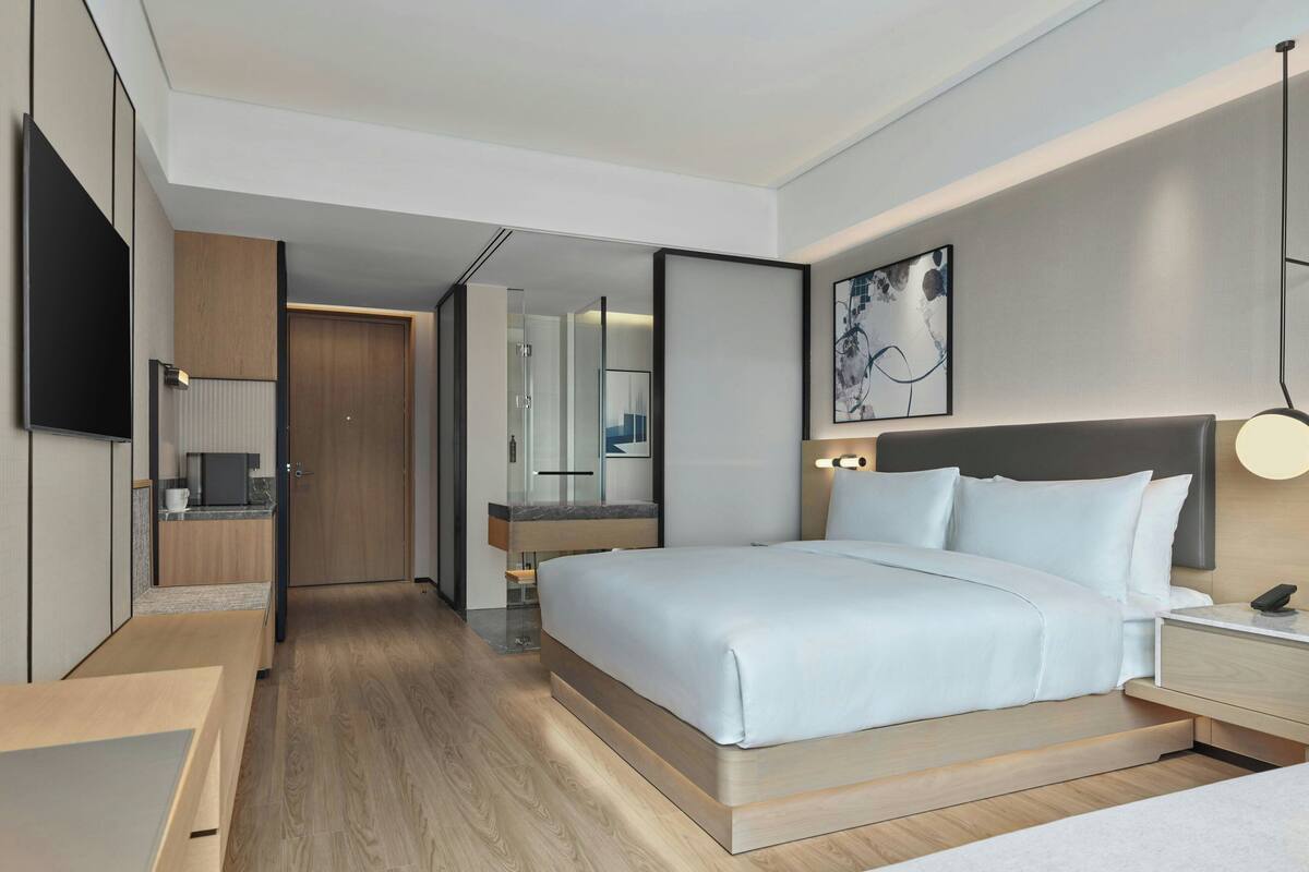 Une chambre d’hôtel moderne dotée d’un grand lit, de tables de chevet, d’un téléviseur à écran plat, d’une salle de bain avec un miroir et d’une petite kitchenette.