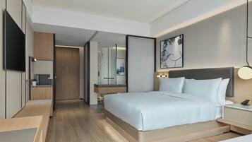 Une chambre d’hôtel moderne dotée d’un grand lit, de tables de chevet, d’un téléviseur à écran plat, d’une salle de bain avec un miroir et d’une petite kitchenette.