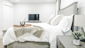 Ein Schlafzimmer mit einem Bett, einem Fernseher, einem Nachttisch mit Lampe und einer kleinen Pflanze.