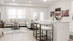 Ein modernes Wohnzimmer mit einer Couch, einem Couchtisch und einer Küchenzeile mit Barhocker und Arbeitsplatte.