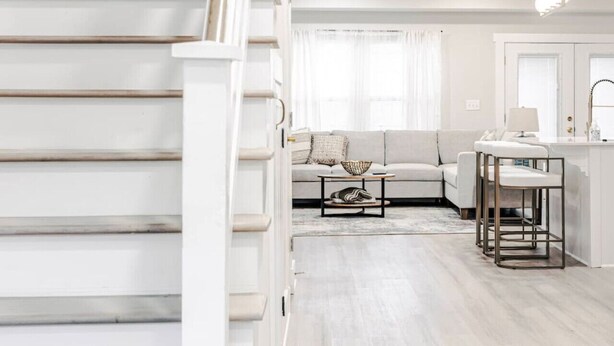 Ein modernes Wohnzimmer mit Treppe, einer Couch, einem Couchtisch und einer Küchenzeile mit Barhocker.