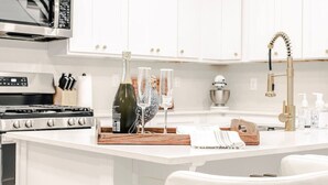 Eine moderne Küche mit weißen Schränken, Edelstahlgeräten und einer zentralen Kochinsel mit Gläsern und einer Flasche.