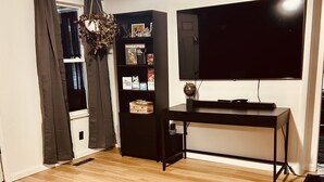 A room with a ceiling fan, a flat-screen TV, a bookshelf, and a large rug on a wooden floor.
