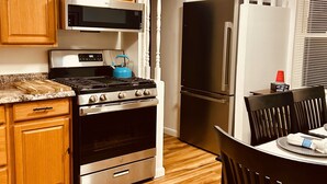 A kitchen with wooden cabinets, a microwave, stove, oven, refrigerator, and a dining table with chairs.