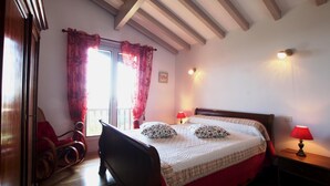 A bedroom with a wooden bed, red curtains, a wooden chair, a nightstand with a lamp, and a window with a view. - SEGURAKO BORDA - URRUGNE (URRUGNE)