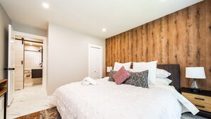 A bedroom with a large bed, wooden panel wall, white bedding, and a nightstand with a lamp.