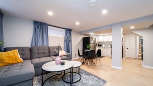 A modern living room with a grey sofa, a coffee table, and a dining area with a black table and chairs.