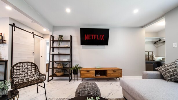 A modern living room with a wooden bench, a sofa, a coffee table, a TV mounted on the wall, and a bookshelf.