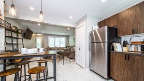 A modern kitchen with a stainless steel refrigerator, wooden cabinets, and a dining area with bar stools.