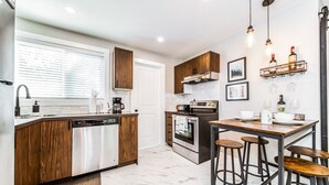 A modern kitchen with a central island, stainless steel appliances, wooden cabinets, and a bar area with stools.