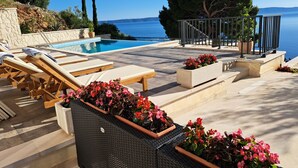 Ein Poolbereich mit Liegestühlen, einer Steinmauer und Blick auf das Meer.