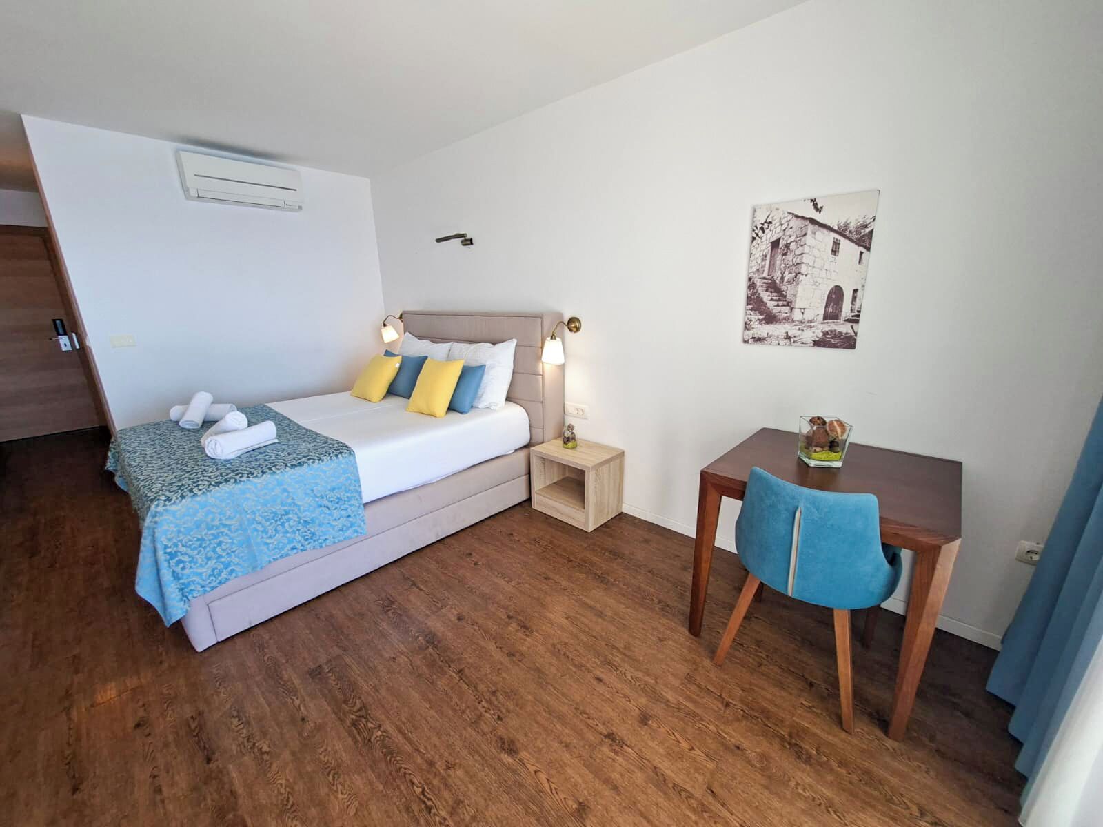 A bedroom with a bed, bedside table, chair, and a small desk.