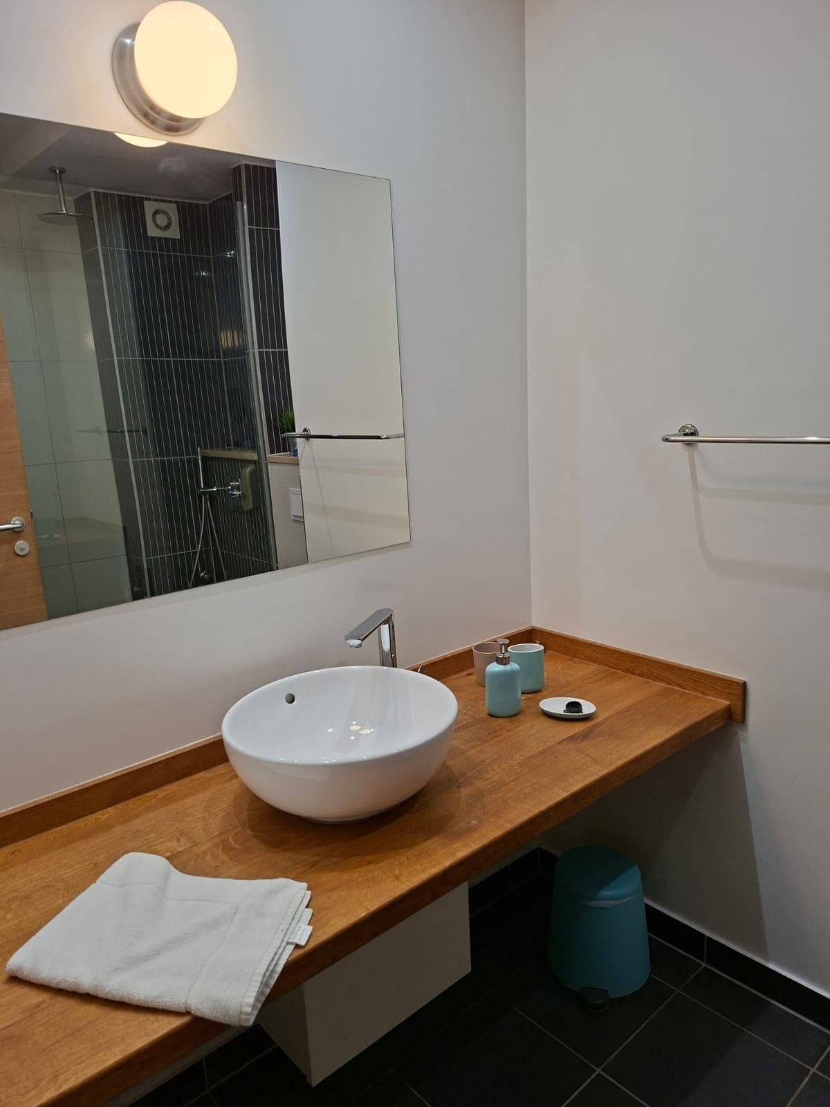 A modern bathroom with a large mirror, a white sink, a wooden countertop, and a towel.