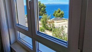 Ein Fenster mit Blick auf das Meer, grüne Vegetation und entfernte Berge.