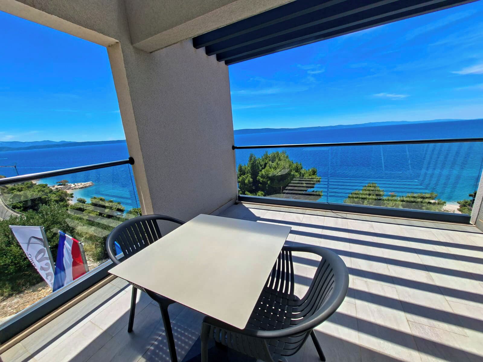 A balcony with a table and chairs, overlooking a coastal view with clear skies.
