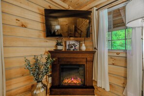 A wooden interior with a fireplace, a mounted television, and a window with curtains.