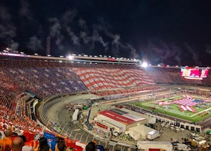 A stadium with a large crowd, a football field, and a prominent American flag display.