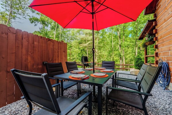 An outdoor patio with a table set for four, surrounded by chairs, and a red umbrella providing shade. - Starry Nights in the Smokey Mountains with Hot Tub Pet Friendly (Elizabethton)