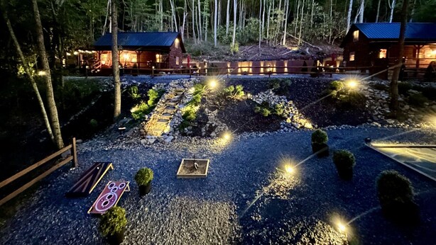A lodge with two cabins, a gravel driveway, and a well-lit garden area.