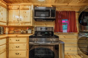 A compact kitchen with a microwave, stove, and oven, wooden cabinets, and a window with curtains. -  Starry Nights in the Smokey Mountains with Hot Tub Pet Friendly (Elizabethton)