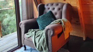 Une pièce chaleureuse avec un décor intérieur en bois, une grande fenêtre, un fauteuil confortable avec un coussin et un téléviseur à écran plat fixé au mur.