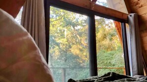 Une pièce dotée d’une grande fenêtre, de poutres apparentes et d’un lit recouvert d’une courtepointe.