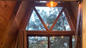 Une pièce chaleureuse avec un plafond en bois, une grande fenêtre, un canapé, une table ornée d’un vase et une échelle.