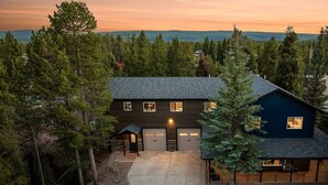 Une maison à deux étages avec un garage, entourée d’une forêt dense.