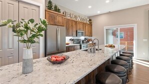 Une cuisine moderne avec des comptoirs en granit, un îlot central doté de tabourets, des armoires en bois et un panneau décoratif représentant le parc de Yellowstone accroché au mur.