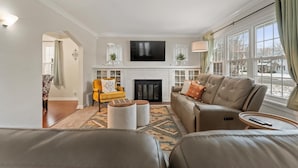 A living room with a fireplace, sofa, armchair, and a television mounted above the fireplace.