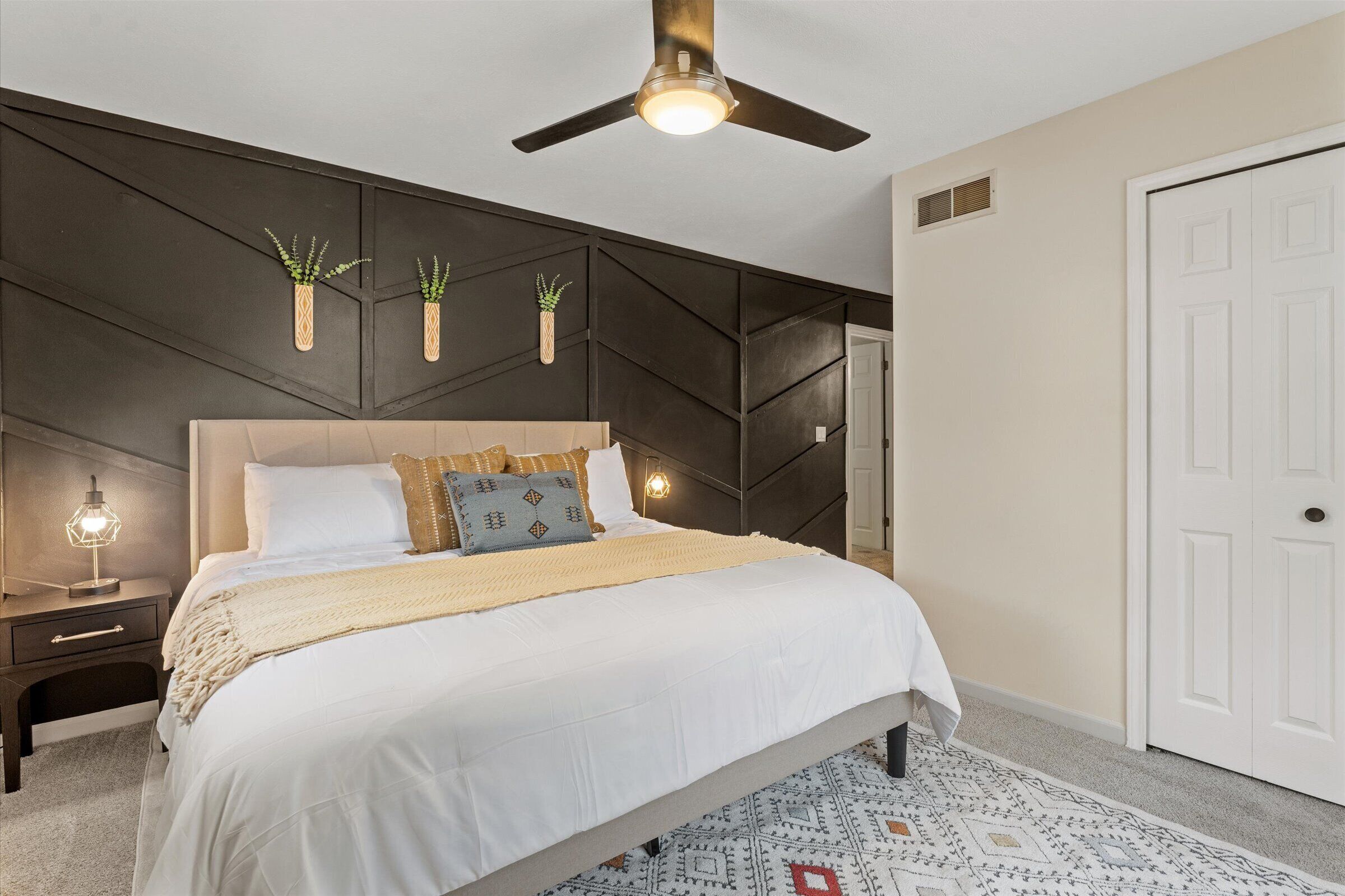 Un dormitorio con cama, mesitas de noche, ventilador de techo y una puerta.