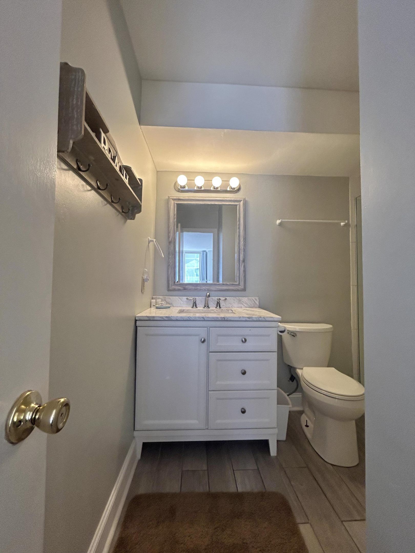 A bathroom with a white vanity, a mirror with lights, a toilet, and a brown rug.