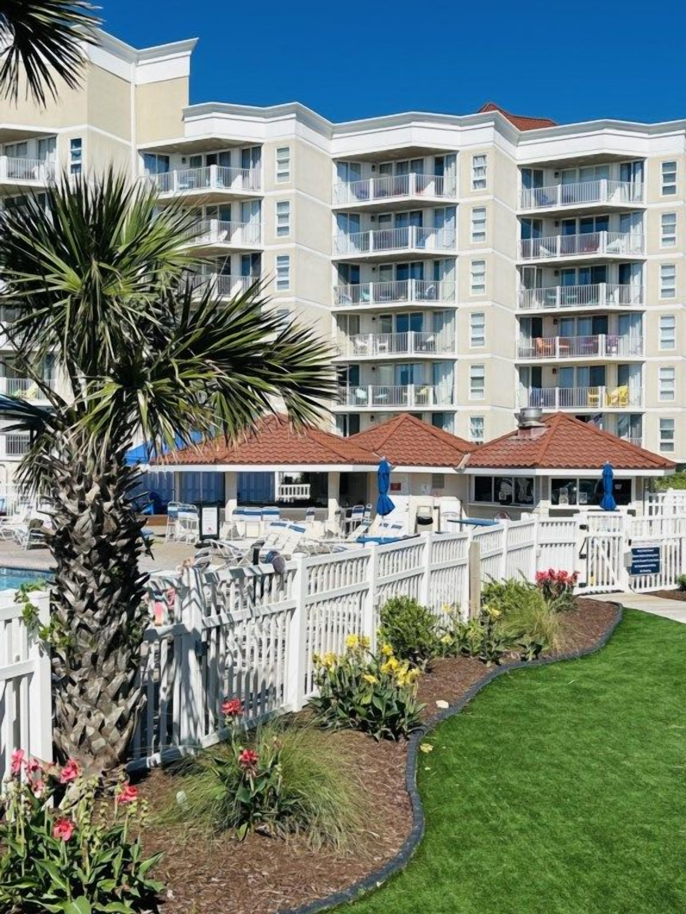 A multi-story hotel with balconies, a swimming pool, and a well-maintained garden.
