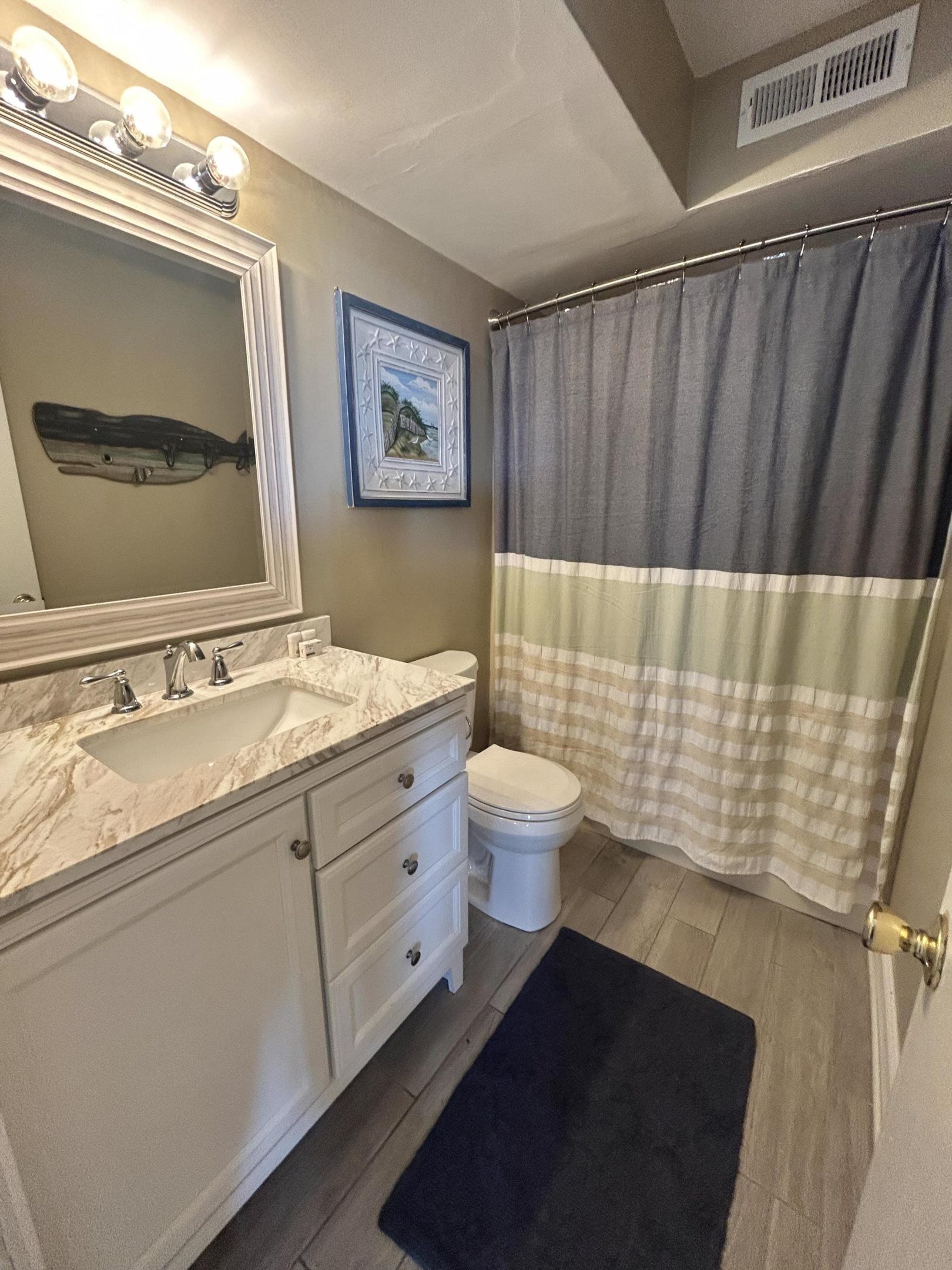 Une salle de bain avec un lavabo en marbre, des toilettes, un tableau encadré au mur et un rideau de douche à rayures.