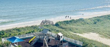 A beachside playground with a basketball court, a slide, and a small building structure.
