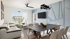 Una sala moderna con un sofá modular, una mesa de comedor con sillas, un televisor de pantalla plana en la pared y un ventilador de techo.