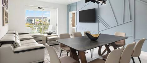 Una sala moderna con un sofá modular, una mesa de comedor con sillas, un televisor de pantalla plana en la pared y un ventilador de techo.
