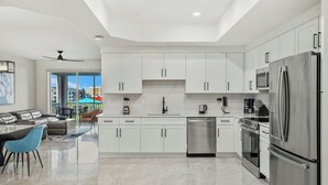 Cocina moderna con armarios blancos, electrodomésticos de acero inoxidable y una zona de comedor con una silla azul.