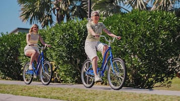 Deux personnes à vélo circulent sur une piste cyclable, avec en arrière-plan de la végétation et des palmiers.