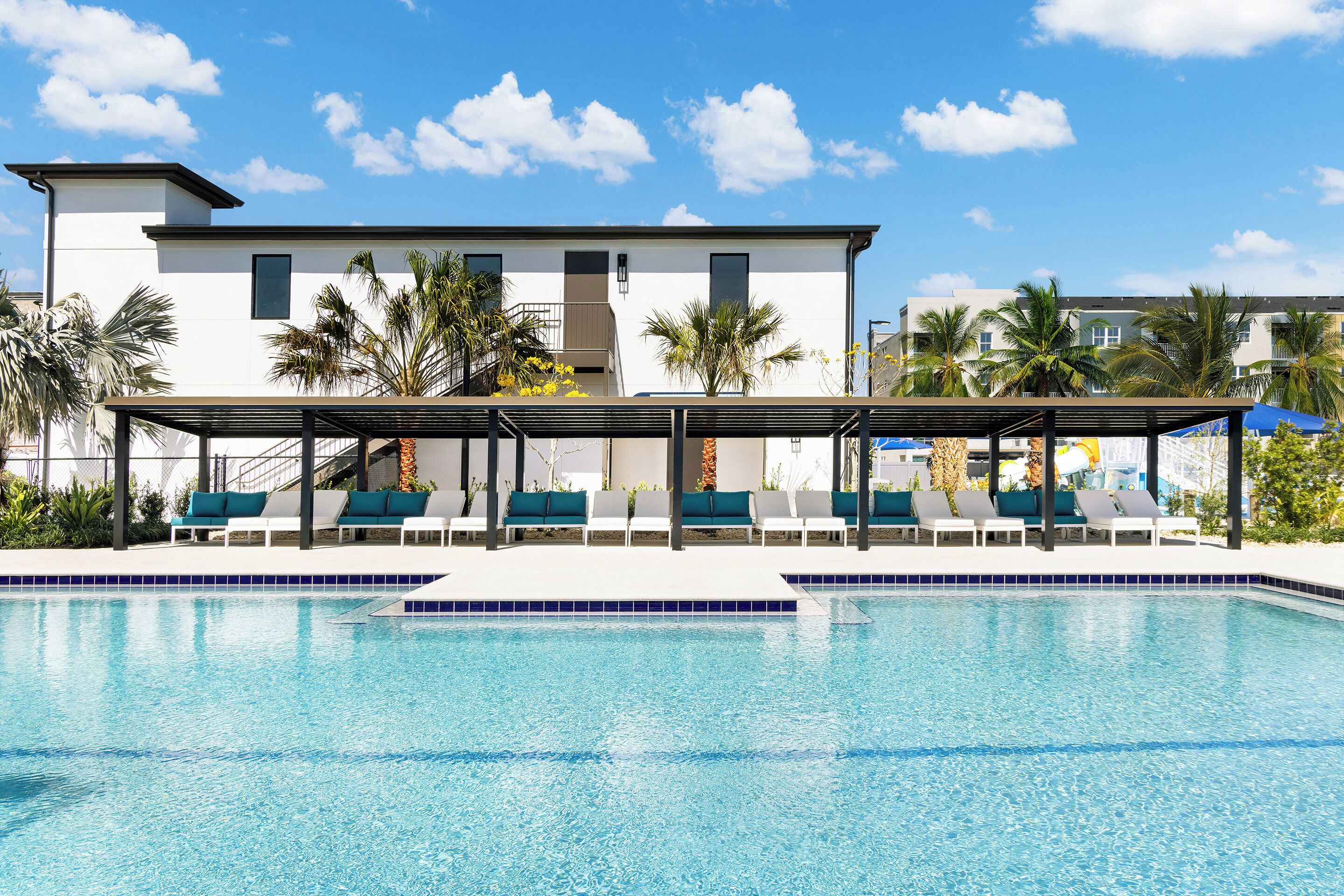 Un hotel moderno con piscina, sillas de descanso y palmeras.