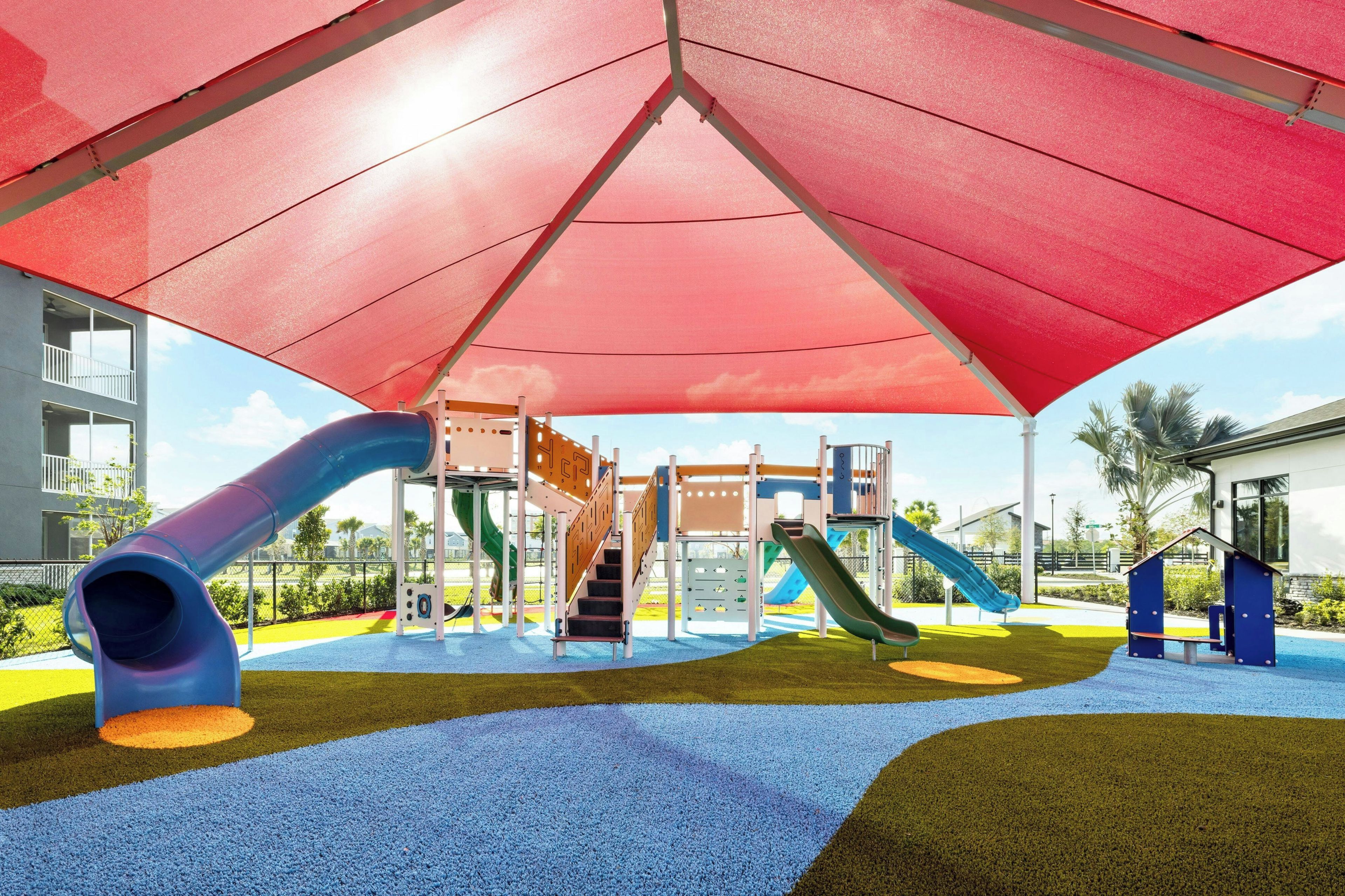 A playground with slides and climbing structures, surrounded by a red canopy.
