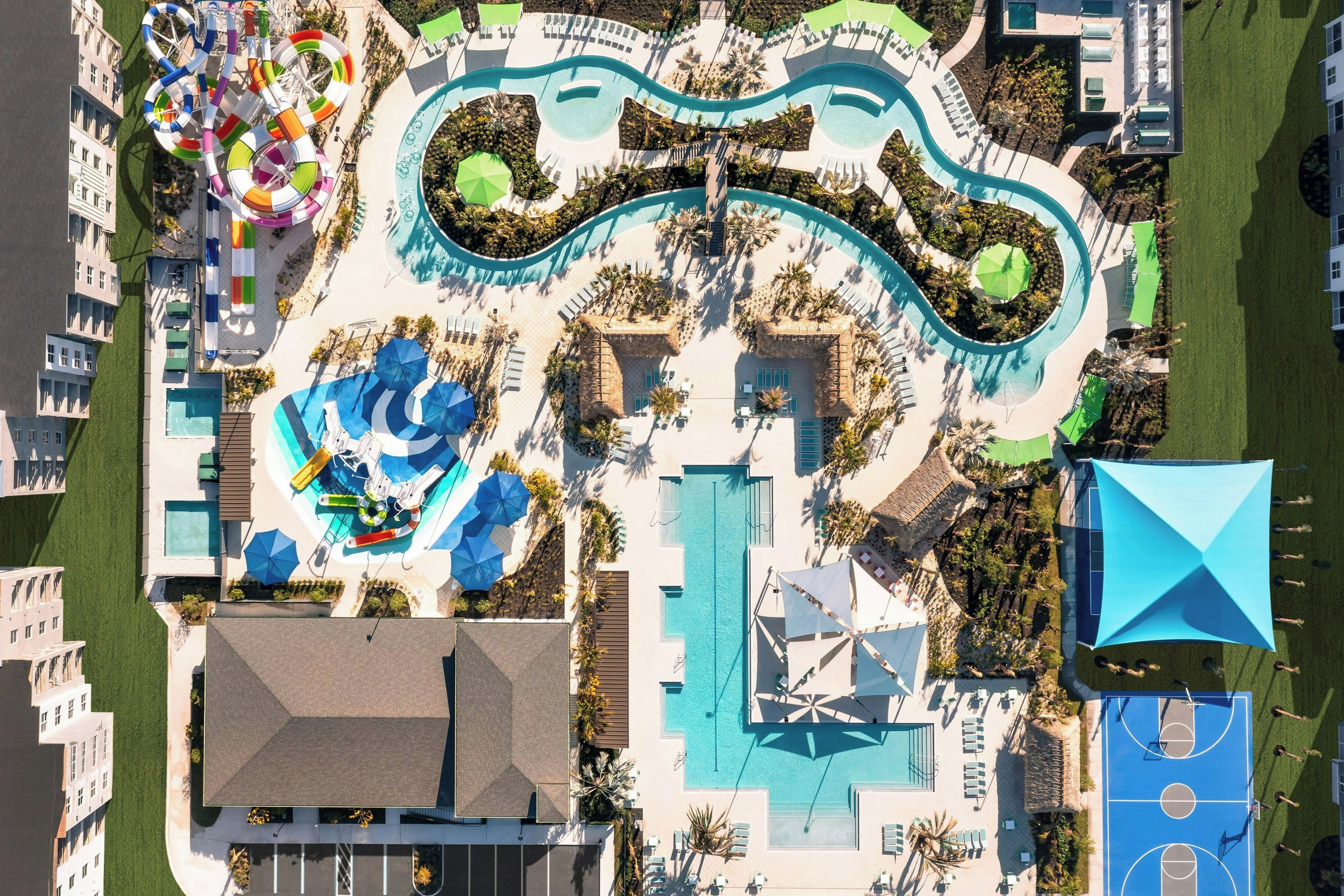 Luchtfoto van een resort met een groot zwembad, glijbanen en een basketbalveld.