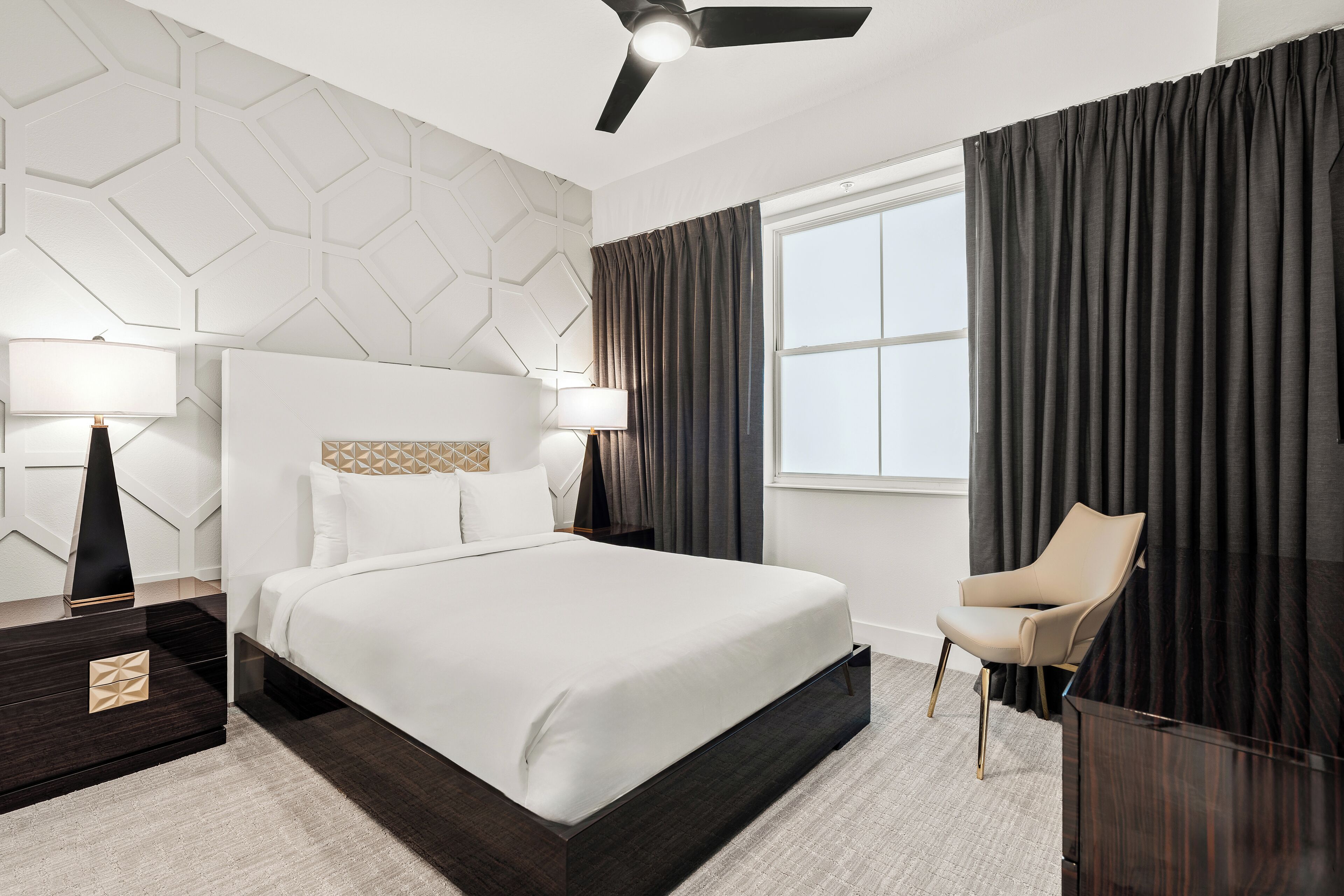Una habitación de hotel moderna con una cama grande, un escritorio, una silla y una ventana con cortinas.