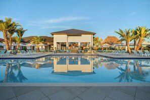 A poolside area with lounge chairs, a building with a flat roof, and palm trees. - Villatel Resort Orlando, Apartments by Marriott Bonvoy (Orlando)