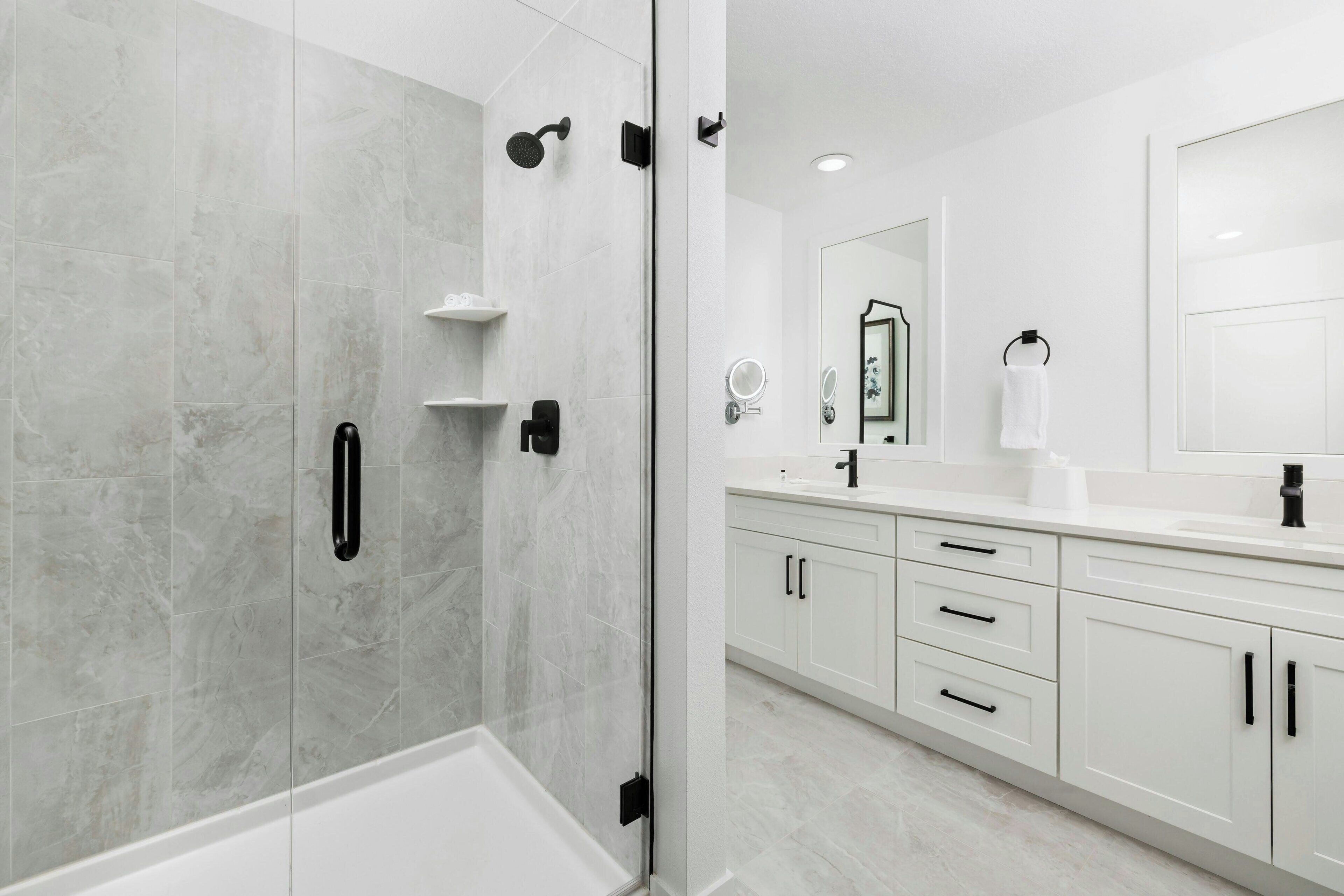 A modern bathroom with a glass-enclosed shower, white cabinetry, and a large mirror.