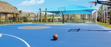 An outdoor basketball court with a blue surface, a hoop, and a net.