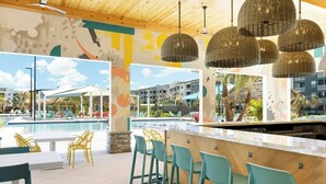 Zona de bar junto a la piscina con iluminación colgante de mimbre, piscina y mobiliario de exterior.