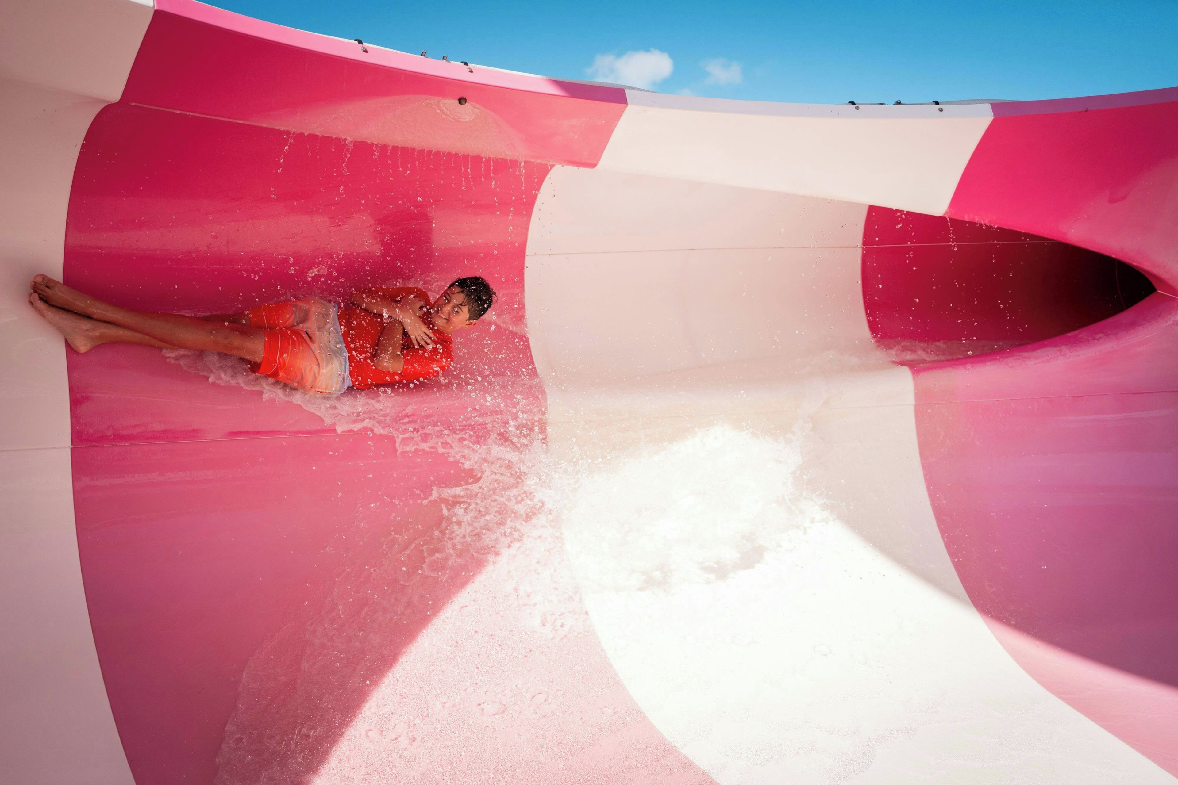 A person sliding down a curved, multi-colored slide with water splashing around.
