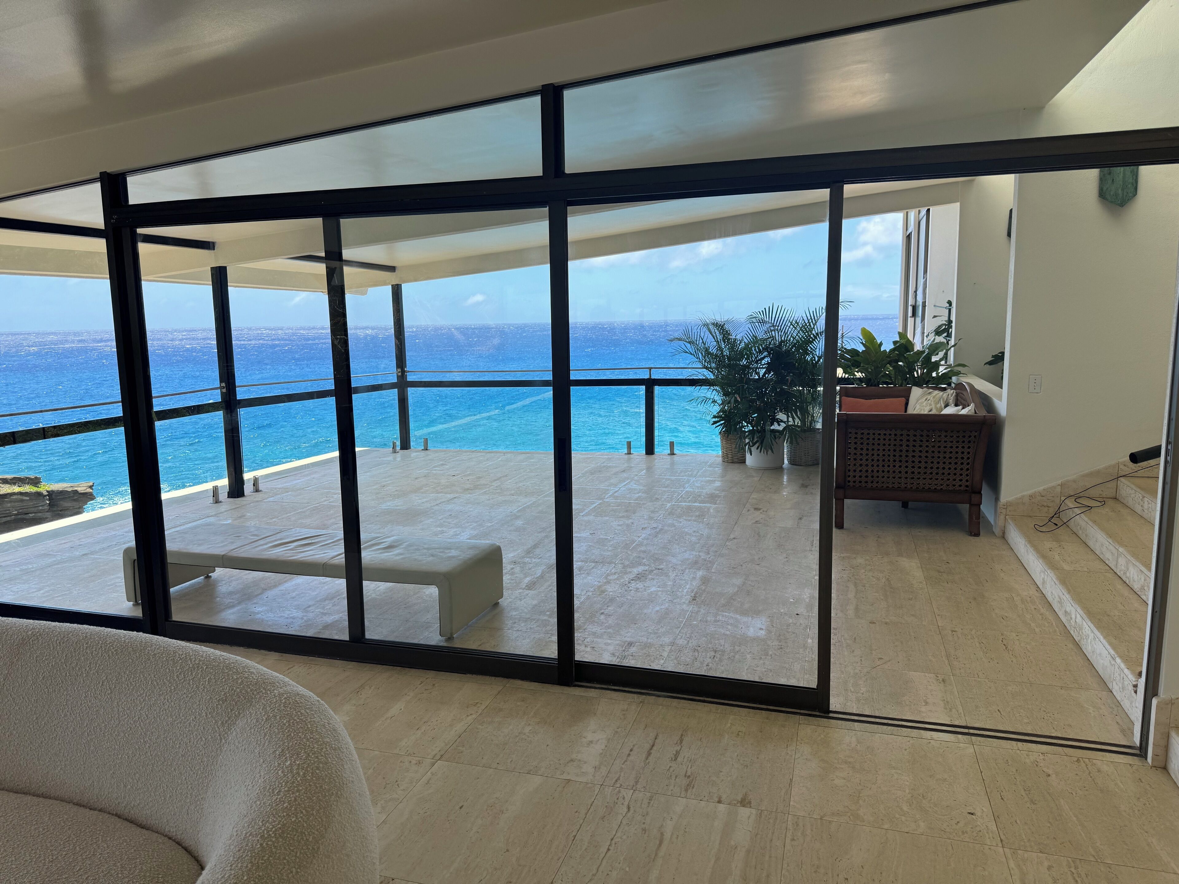 A spacious balcony with a view of the ocean, a seating area, and potted plants.