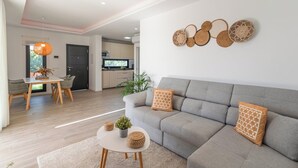 A modern living room with a grey sofa, a dining table with chairs, and a kitchen in the background. - Villa El Rincón de Lupe Torrox by Ruralidays (Málaga)